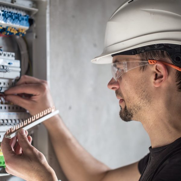 Man, an electrical technician working in a switchboard with fuses. Installation and connection of electrical equipment. Professional with tools in hand. concept of complex work, space for text.